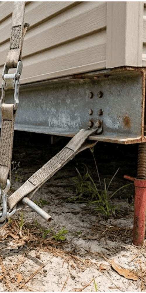 Mobile home tie-down anchor and support strap under the frame