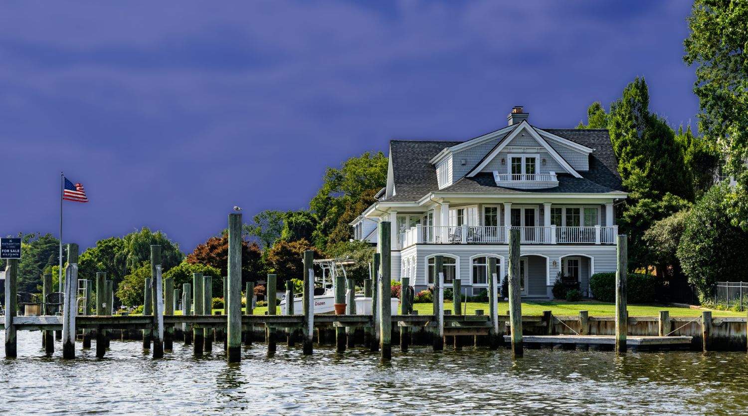 A coastal waterfront home with a wooden boat dock, pilings, and seawall along the water's edge.